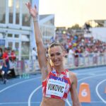 An athlete in a red and white Croatia uniform raises one arm in celebration on a blue track, with spectators visible in the background.